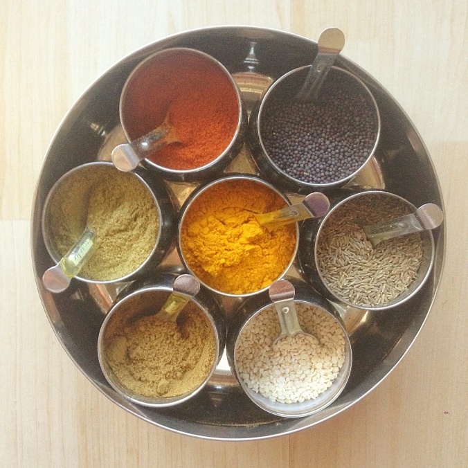 This masala dabba, or spice box, contains our most-utilized Indian spices. Turmeric is front and center, followed by (clockwise): red chili powder, black mustard seeds, cumin seeds, urad dal (a split lentil used in seasonings), cumin powder, and coriander powder. It comes with a glass cover and lid and makes Indian cooking a breeze.